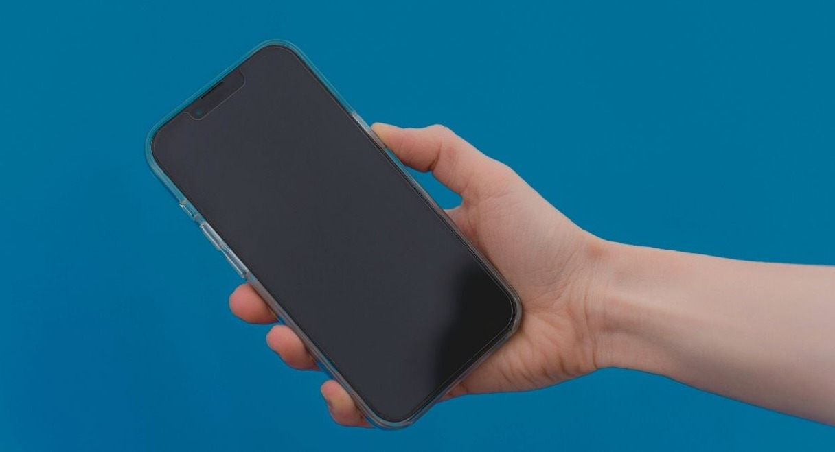 Main tenant un smartphone moderne devant un fond bleu uni