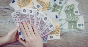 Mains tenant plusieurs billets en euros de differentes valeurs sur une table en bois