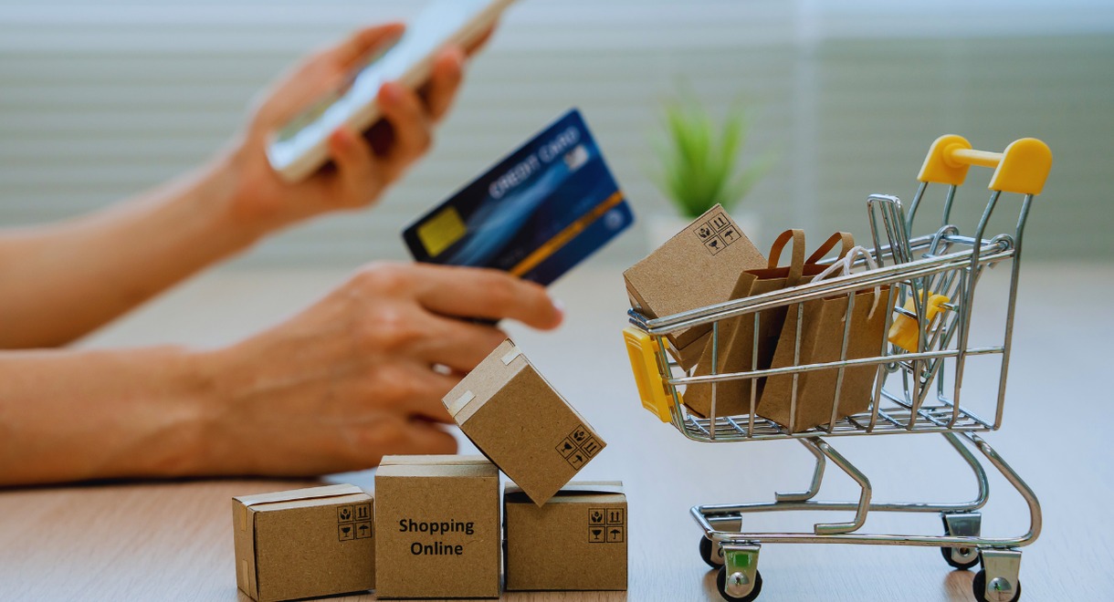 Petits cartons de livraison et mini caddie devant une main tenant une carte bancaire